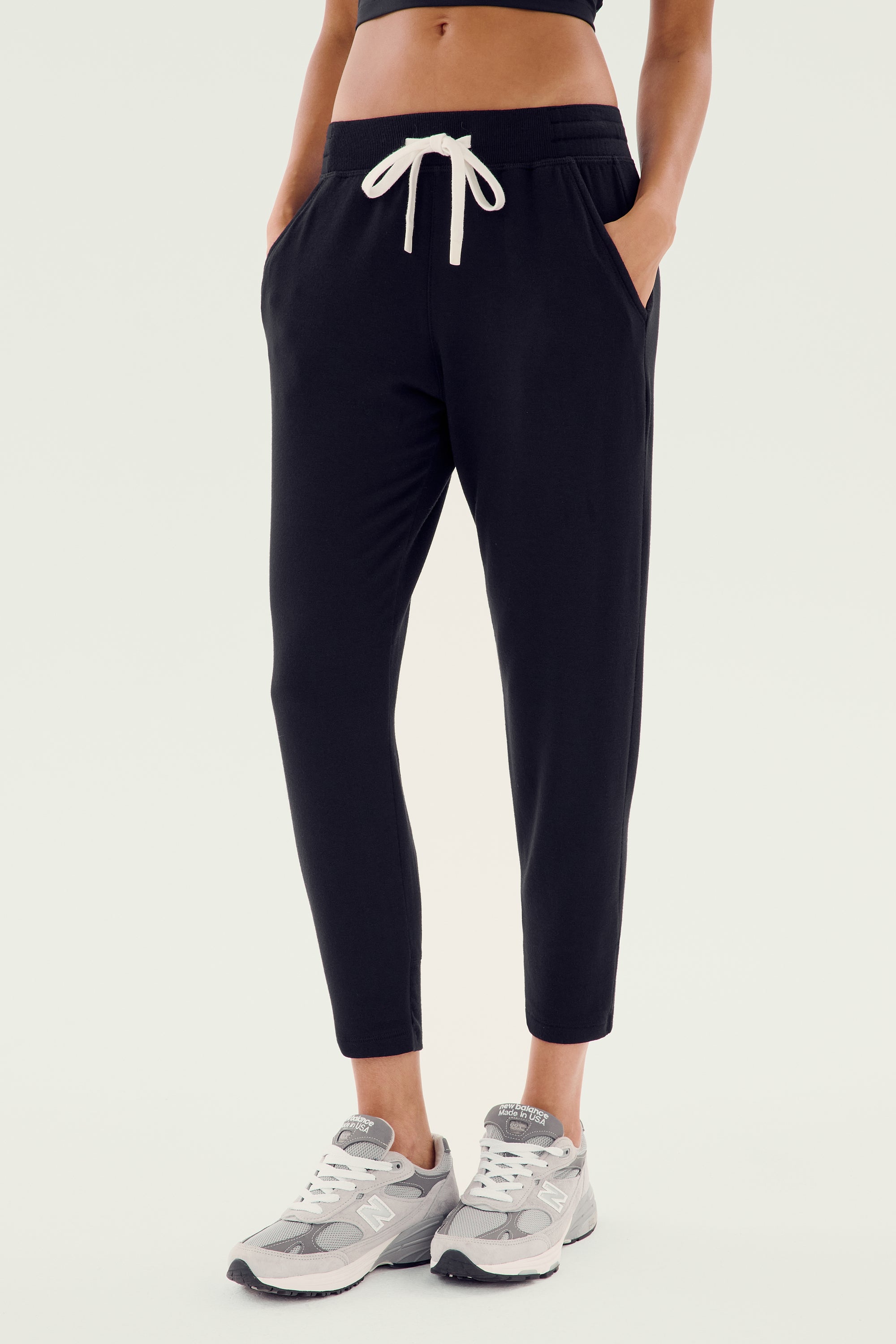 A person wearing the Reena Fleece 7/8 Sweatpant in Black by Splits59, paired with gray sneakers, epitomizes comfort and style.