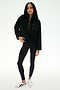 A woman wearing the SPLITS59 Reese Sherpa Half Zip Pullover in black, crafted from 100% polyester, styled with black leggings and white sneakers, stands against a plain white background.