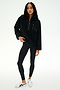 A woman wearing the SPLITS59 Reese Sherpa Half Zip Pullover in black, crafted from 100% polyester, styled with black leggings and white sneakers, stands against a plain white background.