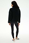 A person stands facing away against a plain white background, wearing the SPLITS59 Reese Sherpa Half Zip Pullover in black (made from 100% polyester), paired with black leggings and white sneakers featuring black stripes.