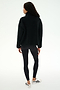 A person stands facing away against a plain white background, wearing the SPLITS59 Reese Sherpa Half Zip Pullover in black (made from 100% polyester), paired with black leggings and white sneakers featuring black stripes.