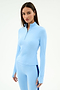 A woman wears the SPLITS59 Tess Rigor Half Zip Waist Length in Skylight—an athletic light blue, long-sleeve nylon-spandex top with a front zipper and matching leggings—standing against a plain white background.