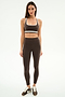 A woman faces forward wearing the SPLITS59 Bianca Rigor Bra in Dark Chocolate/White with matching high-waisted leggings and brown Nike sneakers—an ideal gym workout outfit.