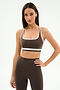 A woman stands against a plain white background wearing the SPLITS59 Bianca Rigor Bra in Dark Chocolate/White with matching high-waisted leggings, an ideal set for high-impact workouts.