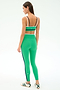 A woman stands facing away, wearing the SPLITS59 Eva Rigor Double Strap Bra in Spearmint/Indigo with matching leggings and white sneakers featuring green stripes.