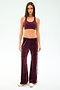 A woman stands facing forward in SPLITS59 Heritage Velour Pant in Dark Cherry/White, paired with a matching burgundy sports bra and beige shoes, set against a plain white background.