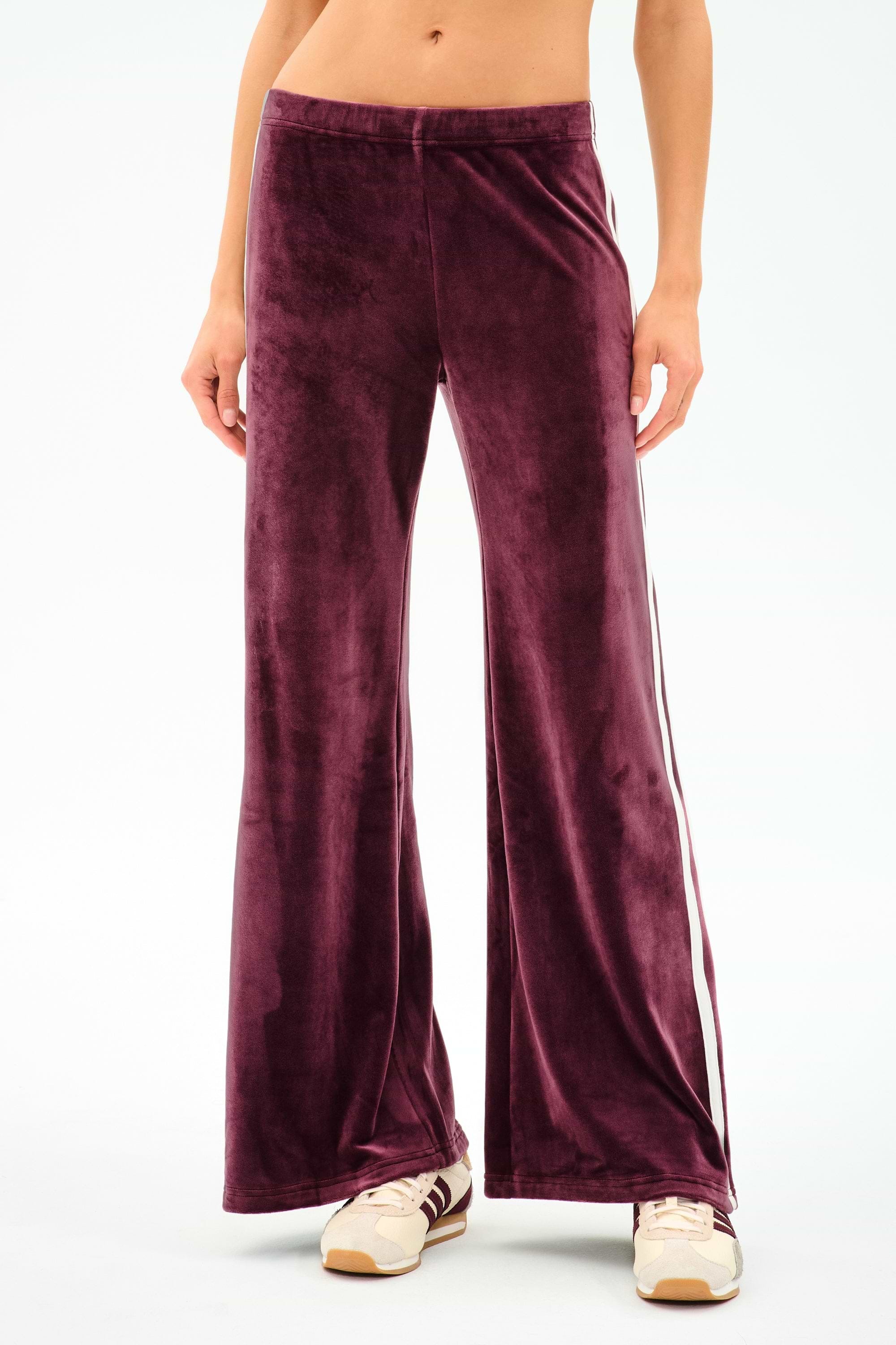 A person wearing SPLITS59 Heritage Velour Pant in Dark Cherry/White, featuring high-waisted, wide-leg design with side stripes and a spandex blend for stretch, paired with beige sneakers against a plain background.