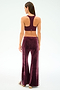 A woman stands facing away, wearing SPLITS59 Heritage Velour Pant in Dark Cherry/White with side stripes and a matching maroon racerback sports bra, crafted from a stretchy spandex blend, against a plain light background.