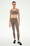 A person stands against a white background wearing the SPLITS59 Margot Rigor Legging in Lentil/Black, crafted from a soft 62% nylon, 38% spandex blend, paired with a matching taupe sports bra and black athletic shoes.