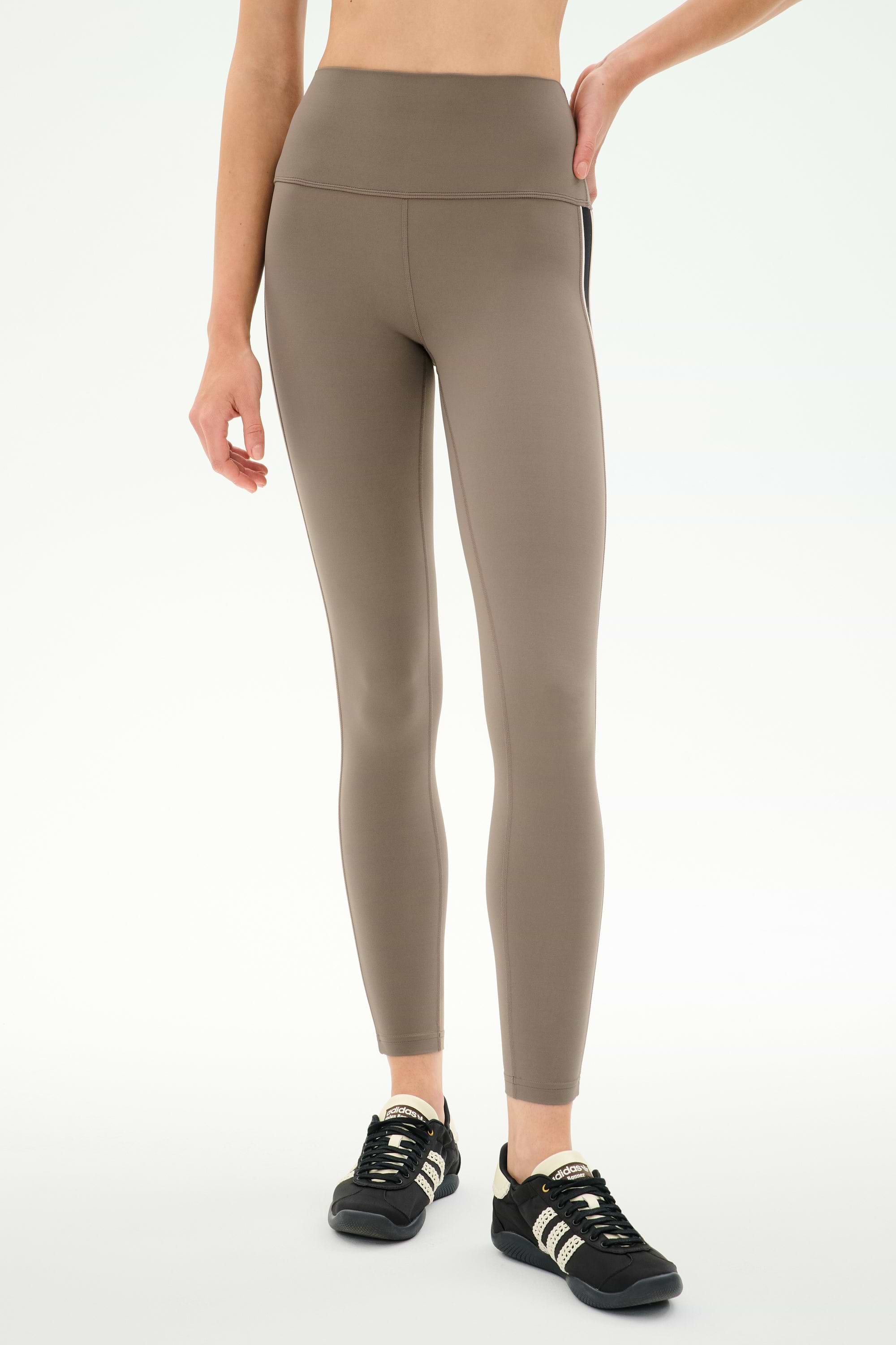 A person wearing SPLITS59 Margot Rigor Legging in Lentil/Black, made from a soft nylon spandex blend, paired with black athletic shoes and standing against a plain white background.