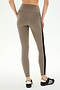 A person wearing the SPLITS59 Margot Rigor Legging in Lentil/Black—a taupe, high-waisted style crafted from a comfortable nylon-spandex blend with a black side stripe—paired with black sneakers, standing against a plain light background.