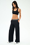A woman stands with hands in pockets against a plain white background, wearing a black sports bra, SPLITS59 Michele Airweight Trouser - Black with a striped waistband, and white sneakers.