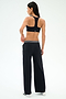 A woman stands facing away, wearing a black sports bra, white sneakers, and SPLITS59 Michele Airweight Trouser - Black with a striped waistband, posed against a white background.
