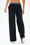 Someone stands facing away, wearing SPLITS59 Michele Airweight Trouser in black with a white-striped waistband and white sneakers against a plain backdrop.