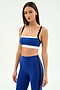 A woman stands against a plain background wearing the SPLITS59 Monah Rigor Bra in Cobalt/Black, paired with matching high-waisted blue leggings featuring black side stripes.