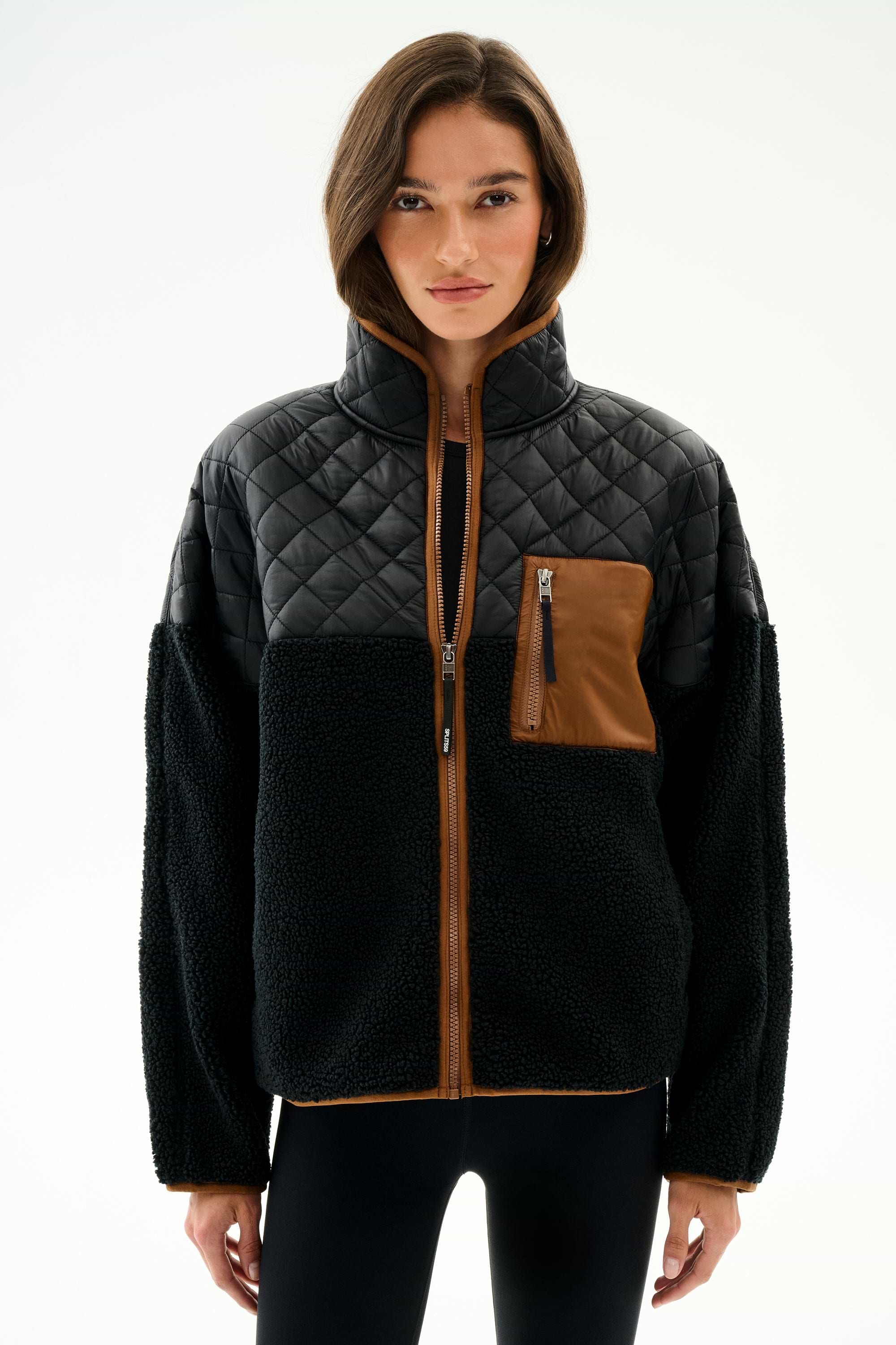A woman wears the Skylar Sherpa Jacket - Black/Toffee by SPLITS59, featuring black fleece, 100% polyester, and brown pocket and trim, against a white background.