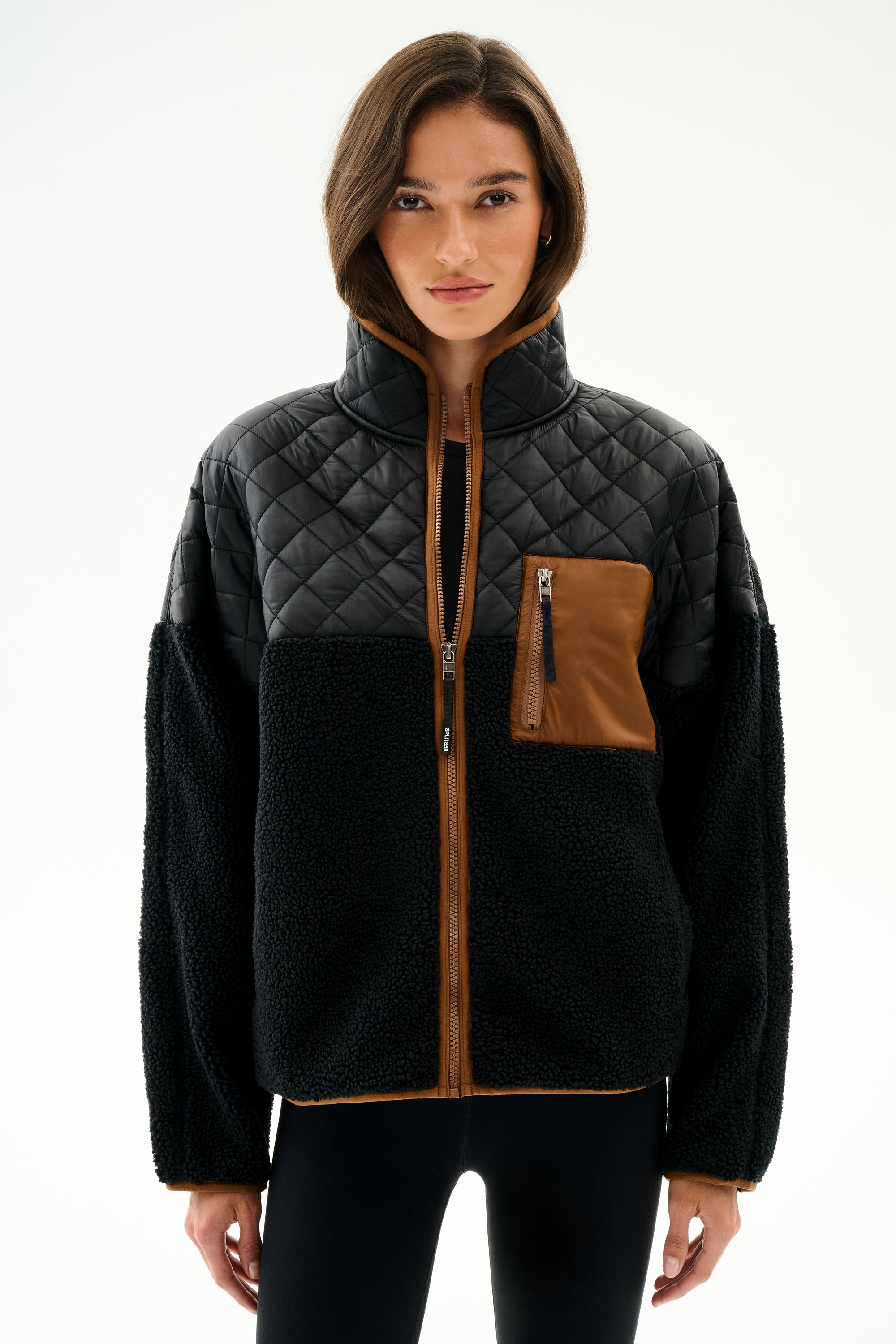 A woman wears the Skylar Sherpa Jacket - Black/Toffee by SPLITS59, featuring black fleece, 100% polyester, and brown pocket and trim, against a white background.