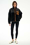 A woman wears the SPLITS59 Skylar Sherpa Jacket - Black/Toffee, paired with black leggings and white sneakers, standing against a white background.