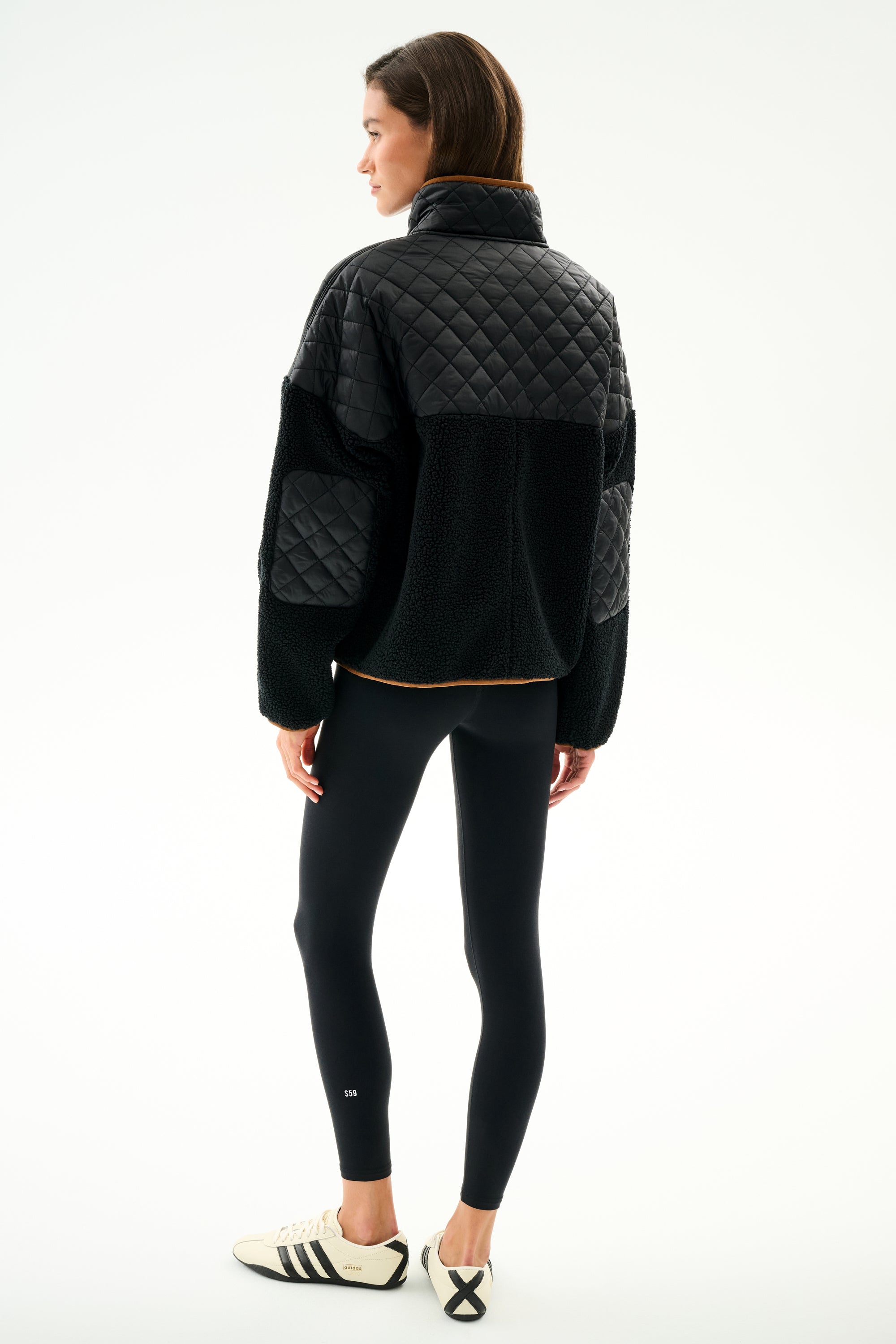 A person stands facing away in a SPLITS59 Skylar Sherpa Jacket - Black/Toffee, black leggings, and white Adidas sneakers with black stripes against a plain white background.