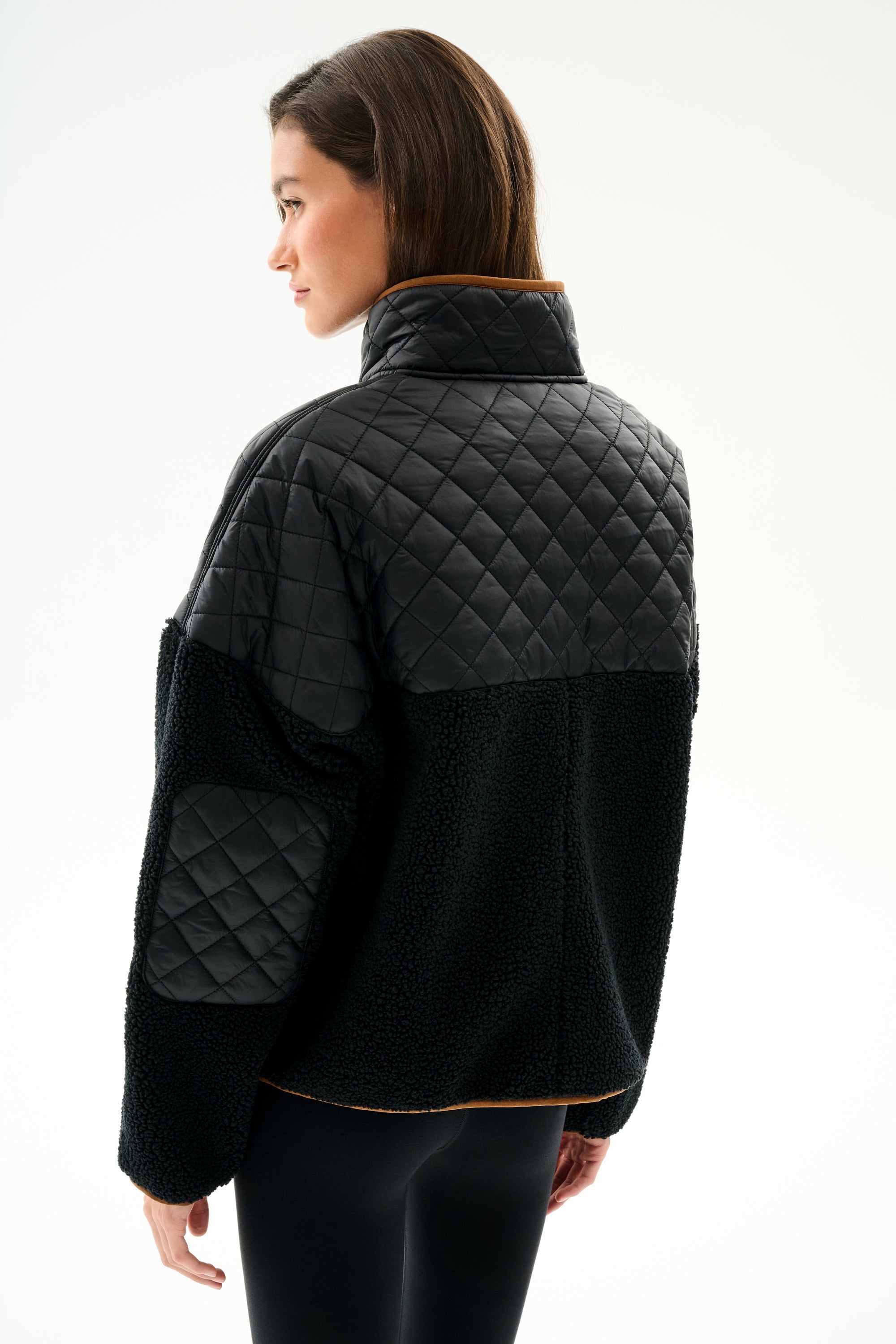 Woman in profile wears the SPLITS59 Skylar Sherpa Jacket - Black/Toffee, featuring a high collar, with black leggings against a plain white background.