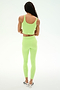A person stands facing away from the camera against a plain white background, wearing SPLITS59's Sprint High Waist Rigor 7/8 leggings in Limeade, styled with a matching light green athletic crop top crafted from stretchy nylon-spandex fabric and paired with white athletic shoes.