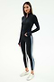 A woman wears the SPLITS59 Tess Rigor Half Zip Waist Length top in black with matching leggings featuring white and blue side stripes, and white sneakers, posed against a plain white background.