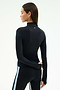 A woman faces away wearing the SPLITS59 Tess Rigor Half Zip Waist Length top in black and sleek black leggings with a light blue side stripe, set against a plain light background.