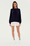 A person standing against a plain background, wearing an SPLITS59 Andie Fleece Sweatshirt - Black made in Los Angeles from stretch modal fabric, white shorts, white socks with black stripes, and white shoes.