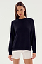 A person with long dark hair stands wearing a SPLITS59 Andie Fleece Sweatshirt - Black and white shorts against a plain background, looking directly at the camera.