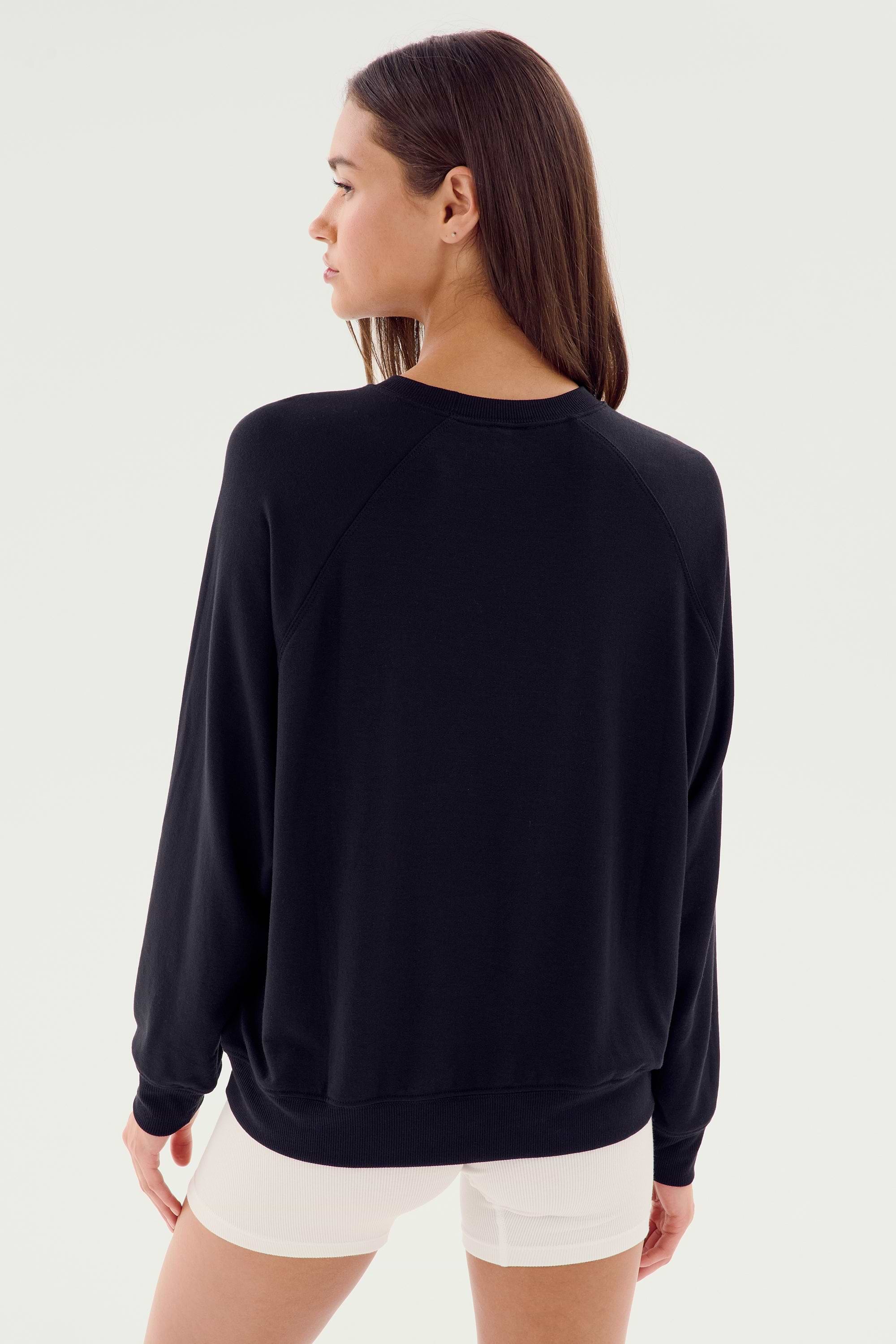 A person with long brown hair wearing an SPLITS59 Andie Fleece Sweatshirt - Black and white shorts made in Los Angeles, facing away from the camera.