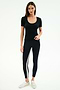 A woman stands against a plain background, wearing the SPLITS59 Ashby Rib Short Sleeve in black, black leggings with a side stripe, and white sneakers.