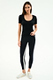 A woman stands against a plain background, wearing the SPLITS59 Ashby Rib Short Sleeve in black, black leggings with a side stripe, and white sneakers.