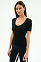 Woman with straight brown hair wearing the SPLITS59 Ashby Rib Short Sleeve top in black, paired with black leggings featuring light blue and white side stripes, standing against a plain light background.