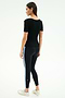 A woman faces away in the SPLITS59 Ashby Rib Short Sleeve—Black, paired with black leggings featuring light blue side stripes and white sneakers, set against a plain light background.