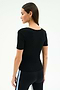A woman faces away in a fitted SPLITS59 Ashby Rib Short Sleeve top in black, paired with black leggings featuring a white stripe—both crafted from soft modal spandex blend—set against a plain light background.