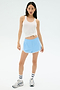 A woman wears the Splits59 Ashby Rib Tank in white, paired with light blue athletic shorts, striped socks, and sneakers, posing against a plain white background.