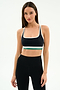 A woman stands against a plain background wearing the SPLITS59 Bianca Rigor Bra in Black/White and high-waisted black spandex leggings.