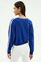 A woman stands with her back to the camera, wearing the SPLITS59 Ellie Fleece V Neck Sweatshirt in cobalt and white, paired with white high-waisted pants for an athletic look.