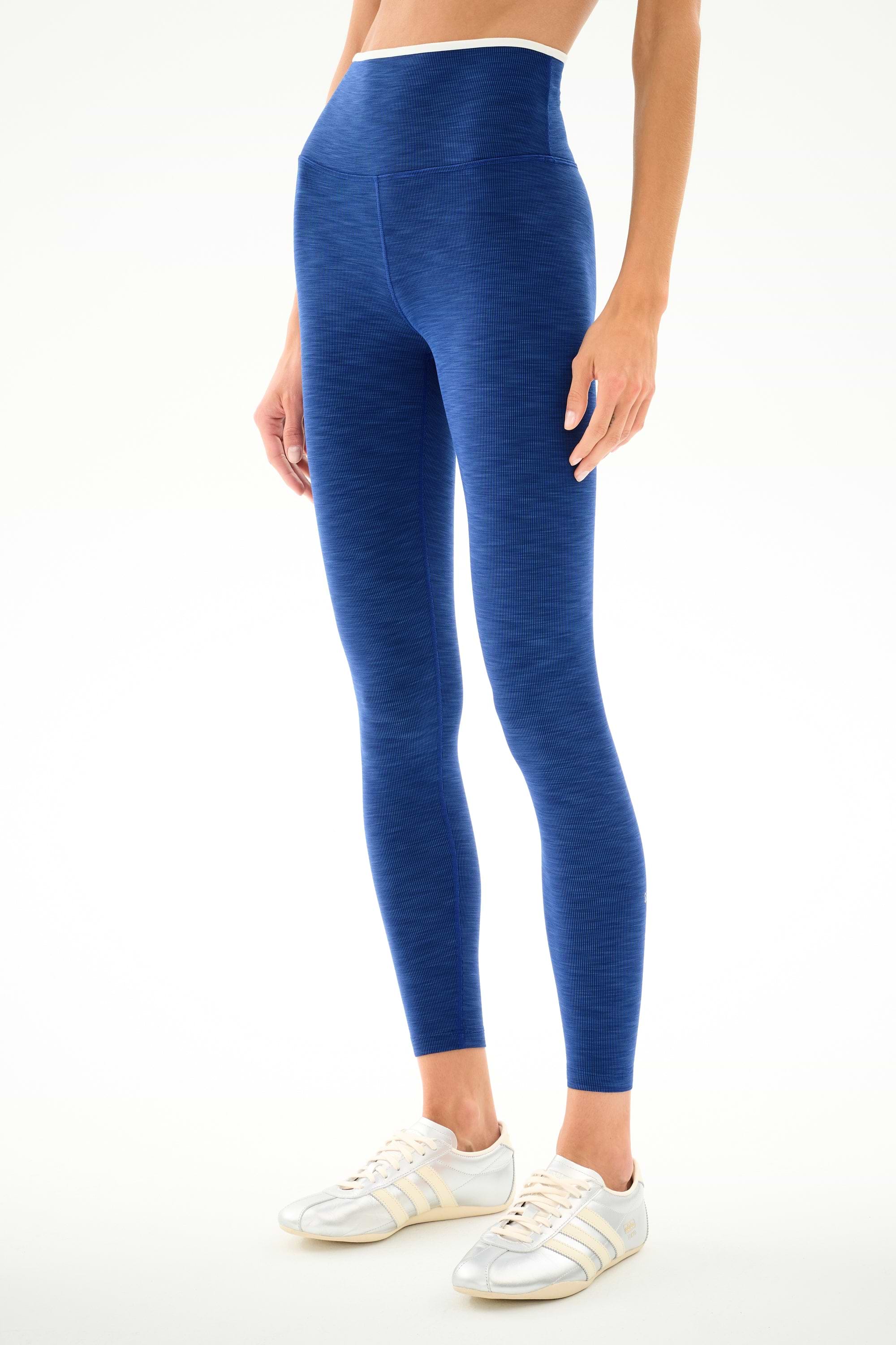Person wears SPLITS59 Hayley Active Rib 7/8 - Heather Cobalt/White leggings and white sneakers, standing against a plain white background.