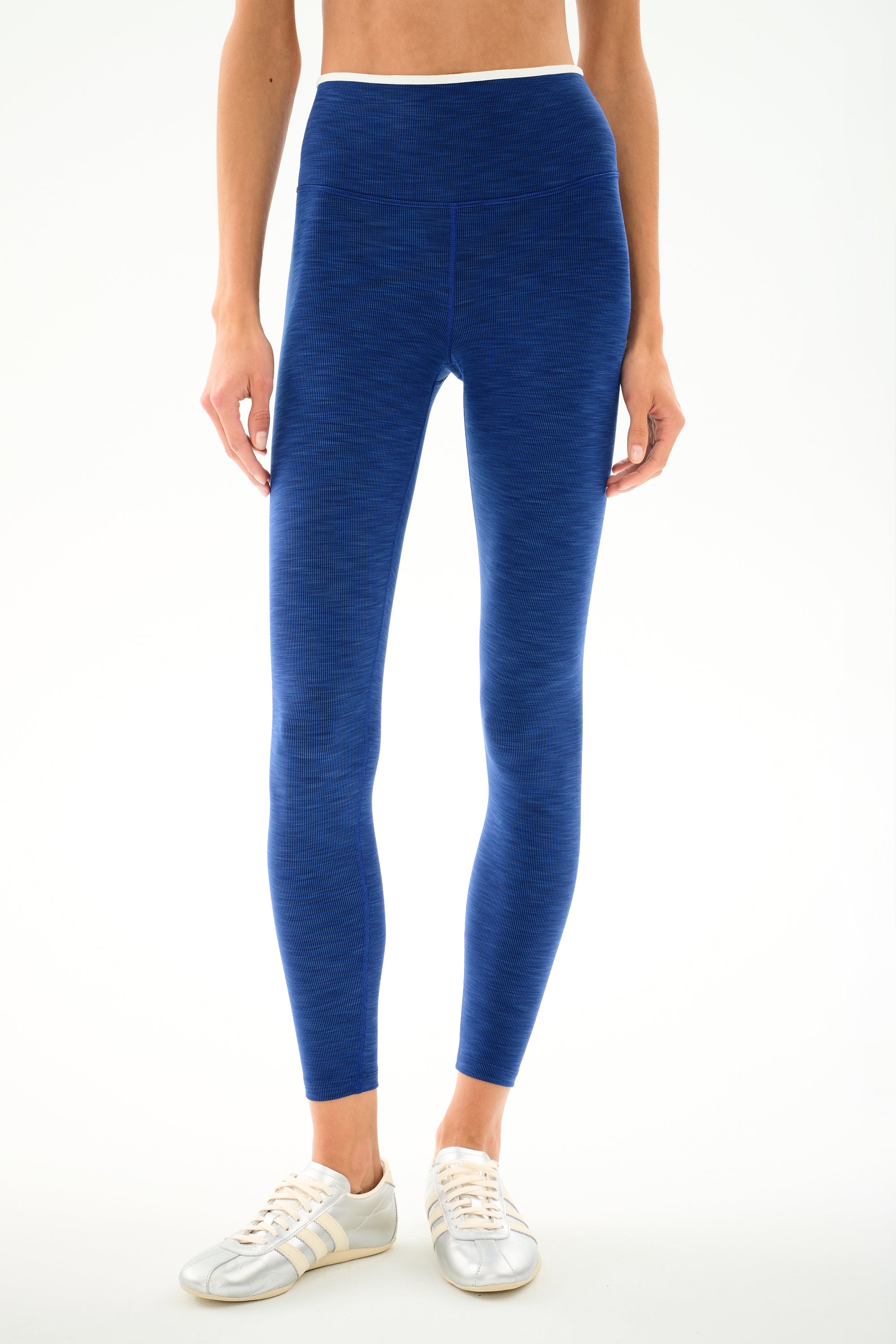 Model wearing SPLITS59 Hayley Active Rib 7/8 - Heather Cobalt/White leggings and white sneakers against a white background, showing only lower torso, legs, and feet.