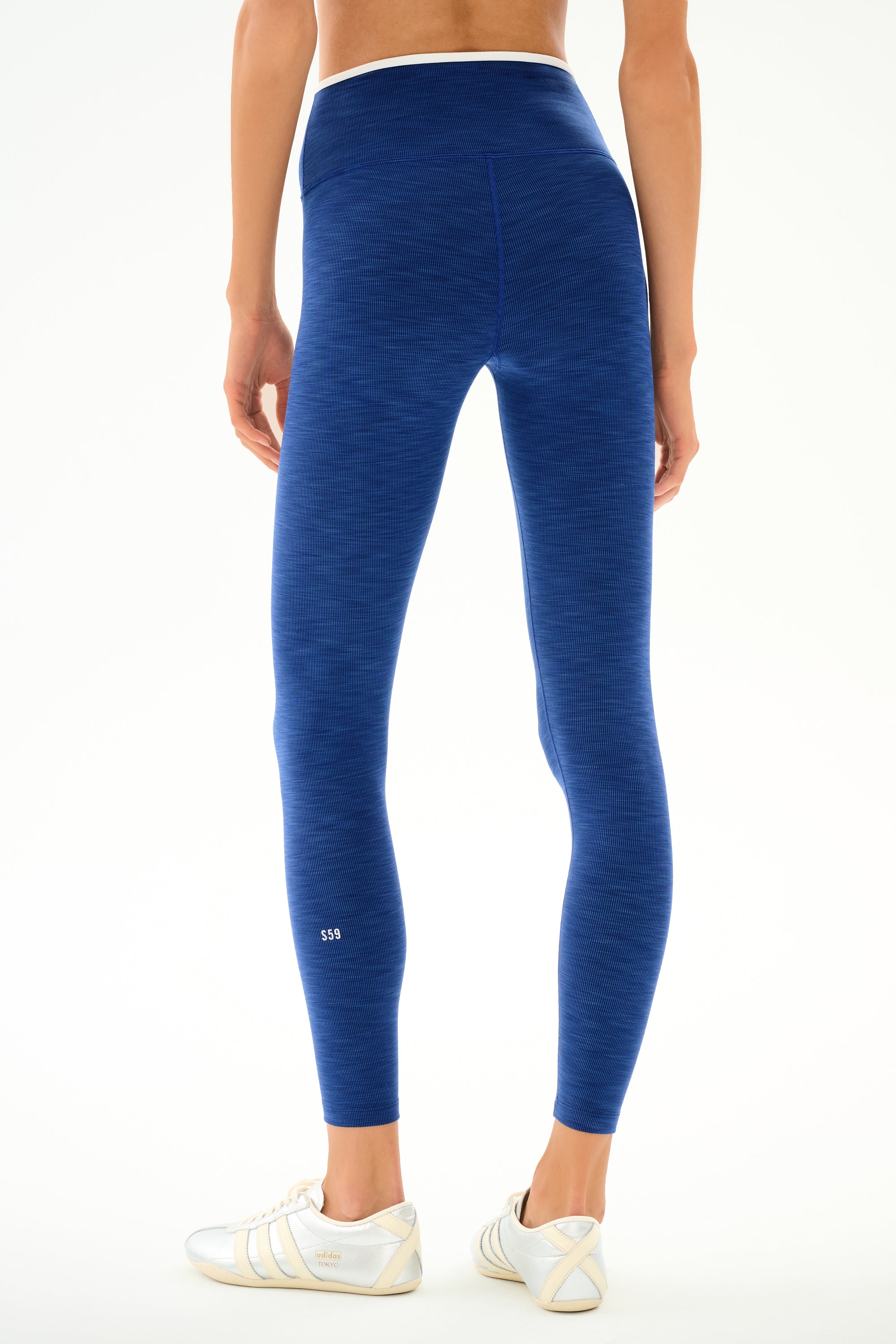 A person stands facing away in SPLITS59 Hayley Active Rib 7/8 - Heather Cobalt/White leggings and white sneakers against a white background.