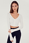 Front view of woman with dark straight hair wearing cropped white four buttoned long sleeve cardigan with thumbholes and dark blue wide bottom leggings