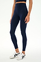 A person stands against a plain white background wearing SPLITS59's Sprint High Waist Rigor 7/8 leggings in Indigo, paired with a navy crop top and white sneakers with black stripes.