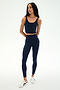 Woman wearing the SPLITS59 Sprint High Waist Rigor 7/8 leggings in Indigo with a matching navy blue athletic crop top, made from Rigor fabric, standing with arms relaxed, looking to the side, and paired with white sneakers on a plain white background.