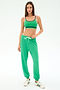 A woman stands facing forward wearing SPLITS59's Andie Oversized Fleece Sweatpant in Spearmint, paired with a green sports bra and white sneakers featuring green stripes.