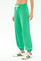 A person wearing SPLITS59’s Andie Oversized Fleece Sweatpant in Spearmint with a white drawstring and white sneakers with green stripes stands against a plain white background.