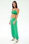 A woman stands against a plain background wearing SPLITS59’s Andie Oversized Fleece Sweatpant in spearmint with a white drawstring, paired with a green sports bra and white sneakers featuring green stripes.