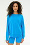 A woman with curly hair wears the SPLITS59 Andie Fleece Sweatshirt in Riviera— a loose, blue crewneck pullover made from soft stretch modal—paired with matching blue shorts, standing against a plain white background.