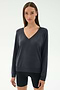 A woman stands against a light background, wearing the SPLITS59 Bennie Fleece V Neck Sweatshirt in Graphite and black shorts. This chic pullover is crafted in Los Angeles.