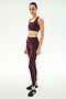 A person stands facing slightly to the side against a plain white background, ready for gym workouts, wearing SPLITS59’s Margot Rigor Legging in Dark Cherry/Black paired with a matching burgundy sports bra and black sneakers.